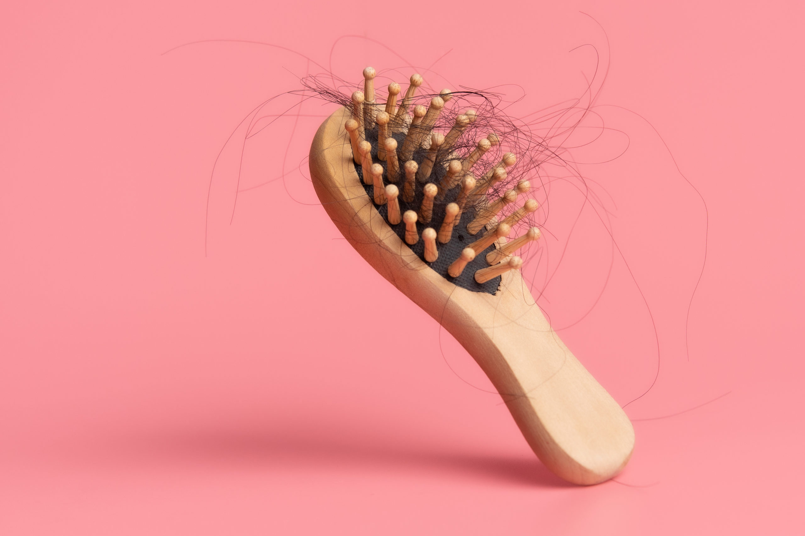 Black hair loss problem with hairbrush on pink background